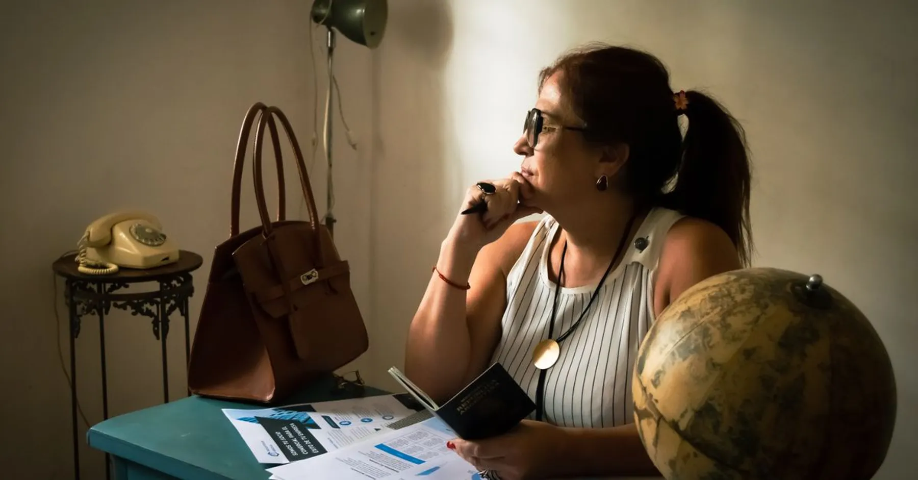 Une femme pensive à un bureau avec un globe, un passeport et des documents