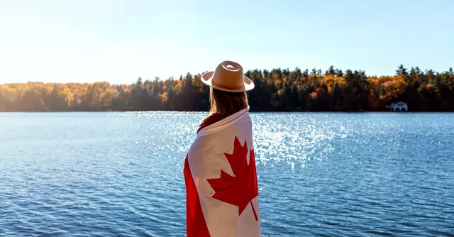 Personne drapée d'un drapeau canadien face à un lac et une forêt d'automne