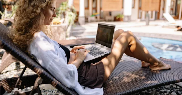 Jeune femme travaillant sur un ordinateur portable au bord d'une piscine