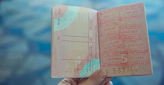 Passeport ouvert couvert de tampons d'immigration, tenu à la main