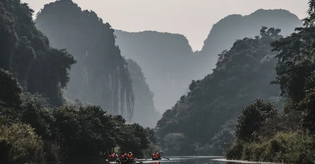 Barques sur une rivière entre des pitons karstiques brumeux, au Vietnam