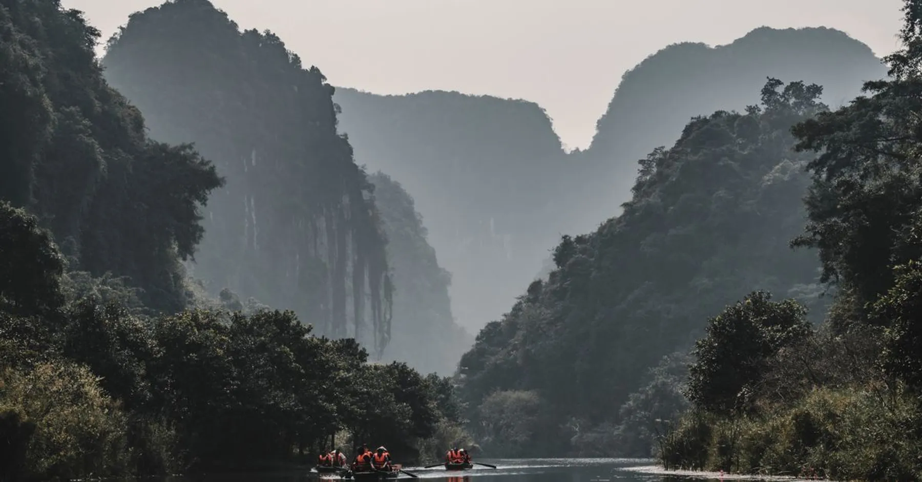 Barques sur une rivière entre des pitons karstiques brumeux, au Vietnam