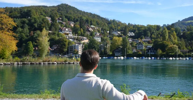 Un homme observe un village suisse au bord d'un lac entouré de collines boisées